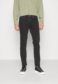 Jeans negros de corte slim y textura suave. Llevados con una camisa de manga larga verde clara y zapatillas altas negras con suelas blancas.