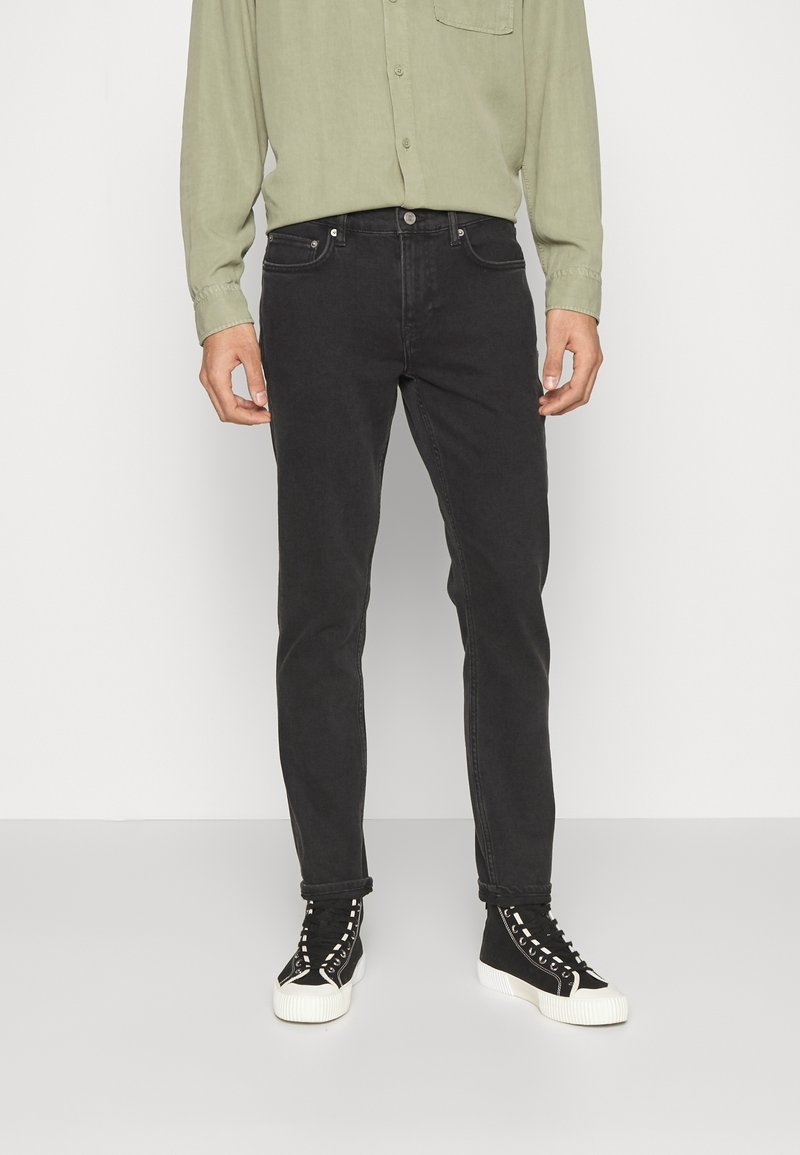 Jeans negros de corte slim y textura suave. Llevados con una camisa de manga larga verde clara y zapatillas altas negras con suelas blancas.