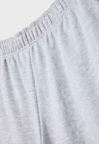 Tessuto grigio chiaro con dettaglio in vita elastica, che mostra una texture morbida e cuciture su un paio di pantaloni o pantaloncini casual.