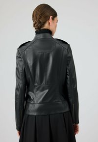 Zwarte leren jas met een aansluitend ontwerp, voorzien van schouderepauletten en ritsmanchetten, met een gladde textuur en op maat gemaakte naden.