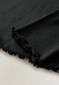 Svart tyg med volangkanter, texturerad yta och mjukt utseende, utlagt platt mot en ljus bakgrund som visar dess flexibilitet.