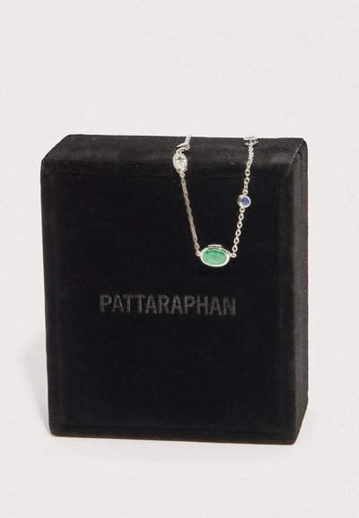 Stříbrný řetízek s přívěsky z zelených, modrých, průhledných a růžových drahokamů vystavený na černé sametové krabičce s nápisem "PATTARAPHAN".
