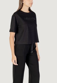 Camiseta negra corta de algodón. Presenta el logotipo "ARMANI" en letras negras texturizadas en el pecho. Manga corta, corte relajado.