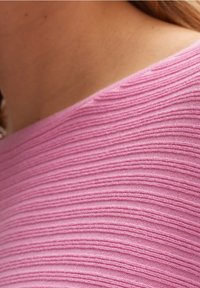 Tissu côtelé rose avec des lignes horizontales, présentant une texture douce et un large décolleté. L'accent est mis sur le motif et les détails du textile.