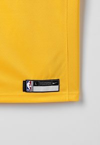 Žlutý tenisový dres NBA v rohu s označením velikosti L, logem Nike a textem "Navrženo podle přesných specifikací šampionátového sportu."