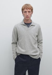 Grijze wollen sweater met een subtiele textuur, voorzien van een kraag en geribde manchetten, gecombineerd met donkere broek. Eenvoudig, neutraal kleurenpalet.