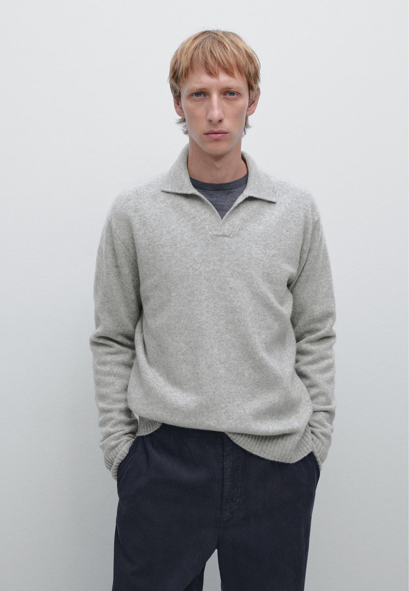 Gray wool sweater with a subtle texture, featuring a collar and ribbed cuffs, paired with dark pants. Simple, neutral color palette.