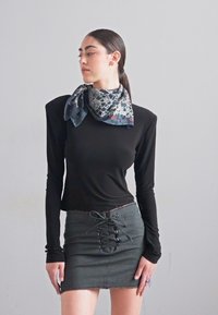 Un top negru cu mâneci lungi, asortat cu o fustă mini gri cu un sistem de șiret la față, accesorizat cu o eșarfă cu model în jurul gâtului.