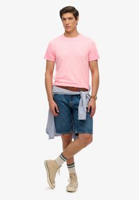 Camiseta rosa de manga corta, pantalones cortos de mezclilla azul, camisa a rayas azul claro atada en la cintura, zapatillas color beige con calcetines a rayas.