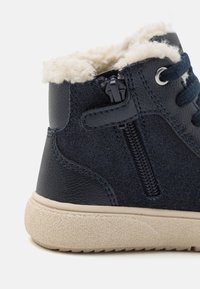 Bota tobillera de marina con parte superior de cuero texturizado y tejido, forro de piel sintética color crema, cremallera lateral y suela de goma texturizada beige.