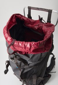 Zaino nero con un cappuccio a corda rossa. Presenta spallacci imbottiti, inserti in rete e numerosi punti di attacco. Tessuto liscio e resistente.