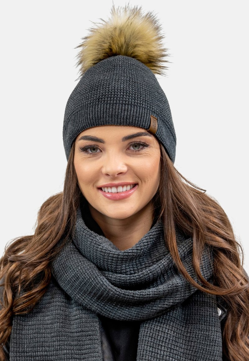 Căciulă tricotată gri cu un pom-pom din blană sintetică de culoare bej deschis, asociată cu o eșarfă texturată gri care se potrivește. Design modern cu plisuri.
