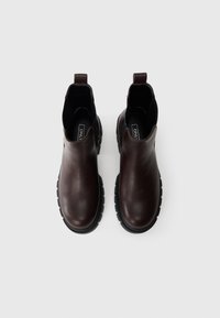 Brune skinnankelsko med chunky svarte såler, elastiske sidestykker og løkke-løkker på hælen for enkel påkledning.