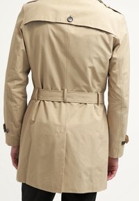 Cappotto beige con vita cintrata, apertura sul retro e dettaglio in bottone sul colletto. Realizzato in un tessuto morbido e leggero.