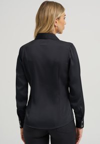 Blusa preta de satin de manga longa com colarinho clássico, punhos abotoados com acabamentos metálicos e um design elegante e ajustado na parte de trás.