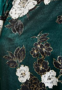 Green textured fabric with a floral pattern featuring white and black flowers, accented by gold outlines and dark green leaves.