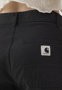 Mustad mustrad tekstuuriga mustad püksid ja tagaküljel tasku, millel on ruudukujuline valge silt logoga. Vöökoht on nähtav.