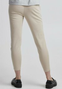 Beige legging gemaakt van zachte, rekbare stof, met een slim fit en een enkel lengte snit. Gepaard met zwarte, platte schoenen.