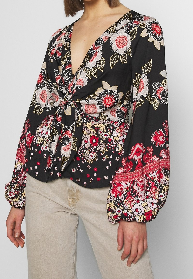Black floral blouse with a deep V-neck, knot detail at the waist, and long puffed sleeves featuring red, white, and yellow patterns.