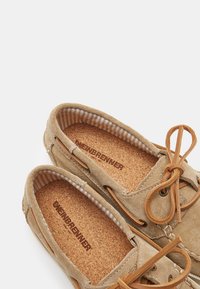 Beige mokasiner i suede med korkinnersåler, med ett randigt tygfoder och lädersnören, som visar en stilren, klassisk design.
