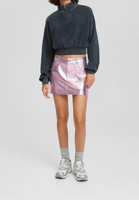 Grå, kort sweatshirt med hög krage, tillsammans med en glansig, rosa minikjol och grå strumpor. Modellen bär grå sneakers.