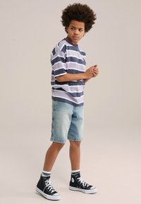 Randig kortärmad skjorta i marinblått och vitt, tillsammans med ljusa denimshorts. Svarta hög-top sneakers med vita sulor och randiga strumpor.
