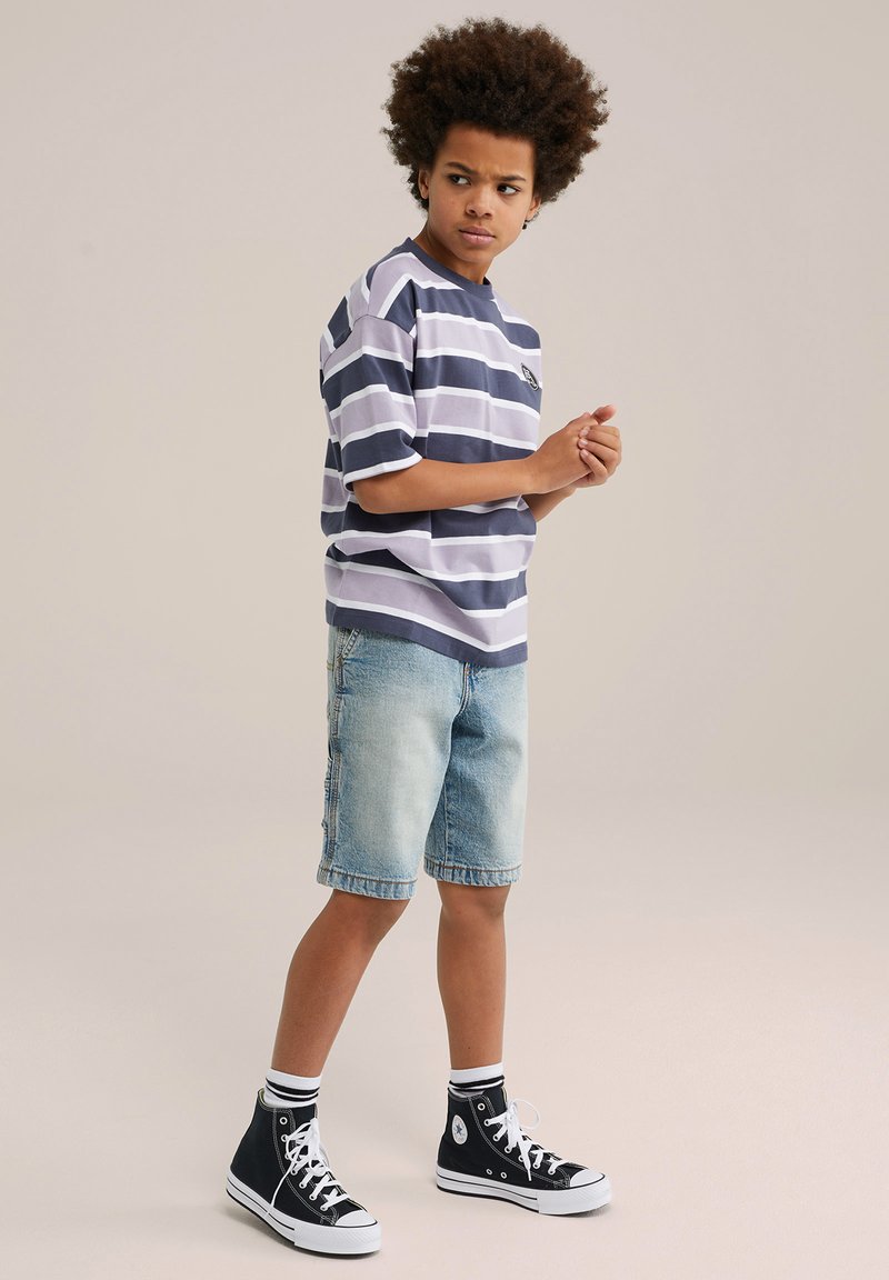 Randig kortärmad skjorta i marinblått och vitt, tillsammans med ljusa denimshorts. Svarta hög-top sneakers med vita sulor och randiga strumpor.