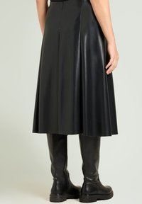 Sort lædernederdel med flared design, der har en lynlås bagpå og en glat, skinnende tekstur. Kombineret med knæhøje sorte læderstøvler.