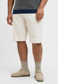 Lys beige shorts med en afslappet pasform, der er parret med grå sokker og lysebrune ruskinds sko. Overdelen har et struktureret gråt strikket design.
