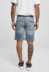 Lysblå denimshorts med en falmet vask, afsluttet med en rå kant. Har to baglommer og en tan læderpatch ved taljen.