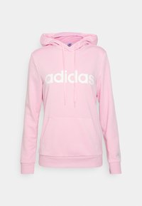 Różowa bluza z kapturem, posiadająca przednią kieszeń oraz białe logo "adidas". Posiada kaptur ze sznurkami, ściągacze przy rękawach oraz miękką teksturę materiału.