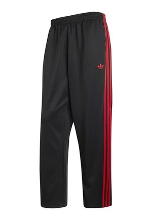 Mustat urheiluhousut joustavalla vyötäröllä, joissa on kolme pystysuoraa punaista raitaa ja punainen Adidas trefoil -logo sivulla.