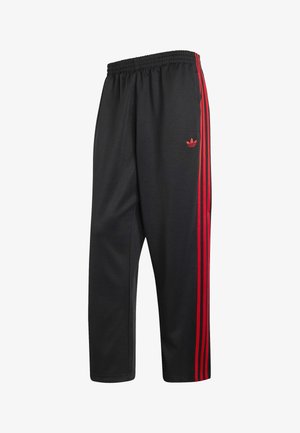 Mustat urheiluhousut joustavalla vyötäröllä, joissa on kolme pystysuoraa punaista raitaa ja punainen Adidas trefoil -logo sivulla.