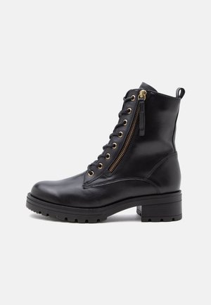 Bottine noire en cuir avec lacets sur le devant, fermeture éclair latérale, bout rond, semelle épaisse et talon bas et épais sur fond blanc.
