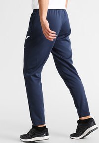Marineblå sportsbukser, tætsiddende design, elastisk talje, sidelommer, lavet af letvægtsstof. Båret med sorte strukturerede sneakers.