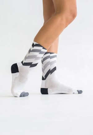 Weiße und graue Socken mit einem Zickzackmuster, versehen mit schwarzen Akzenten und einer verstärkten Zehenpartie. Strukturierter Stoff mit einem unterstützenden Sitz.