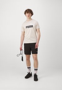 Valge T-särk musta "PUMA" logoga, mustad lühikesed püksid ja mustad tossud. Seljas triibulised valged ja mustad sokid, hoiab hüppenööri.
