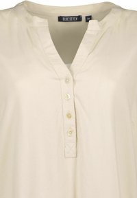 Camicetta color crema chiara in button-up di Blue Seven, caratterizzata da un colletto, cinque bottoni perla e una texture liscia e leggermente lucida.