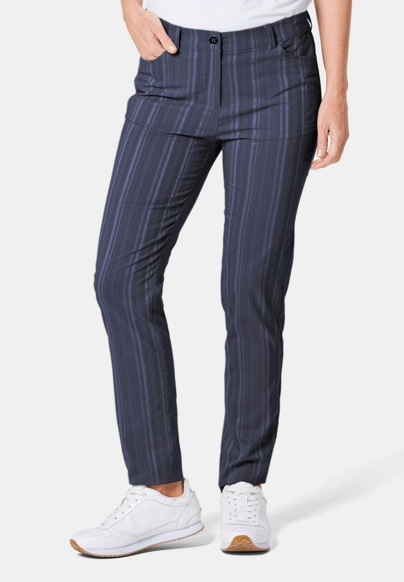 Marineblauwe broek met strepen in een lichtgewicht, gladde stof. Voorzien van een ritssluiting, voorzakken en een getailleerde pasvorm. Draagt wit sneaker.