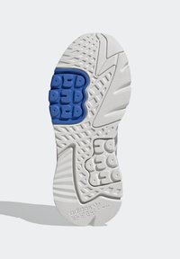 Biała sole sneakerów z teksturowanym wzorem, niebieskim akcentem z gumy o wypukłych sekcjach oraz małym logo na pięcie.