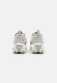 Graue und weiße Sneakers mit einem strukturierten Design, ausgestattet mit einem rosa Nike-Logo, einer Zuglasche und einer klobigen Sohle mit ausgeprägtem Profil.