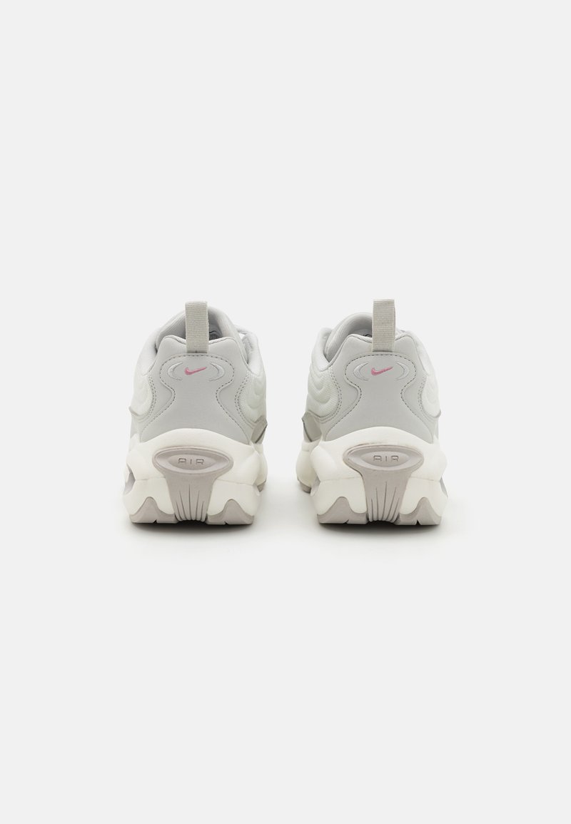 Scarpe da ginnastica grigie e bianche con un design testurizzato, dotate di un logo Nike rosa, una linguetta sul tallone e una suola spessa con scanalature ben definite.