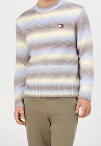 Pull rayé multicolore en tissu tricoté doux, avec des nuances de bleu, jaune et marron. Poignets et ourlet côtelés, avec un petit patch logo.