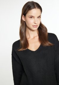 Pulover negru tricotat cu un design în formă de V, cu un fit ușor lejer și mâneci lungi. Textură moale cu detalii subtile de nervuri.
