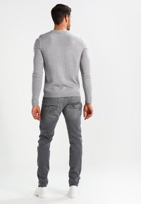 Grauer gestrickter Pullover mit gerippten Bündchen und Saum, kombiniert mit grauen Jeans mit dezenten Gesäßtaschen. Modell von hinten gezeigt, trägt weiße Sneaker.