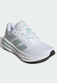 Baskets de sport blanches avec des rayures gris clair, tige en mesh, lacets blancs et semelle rembourrée avec embout noir.