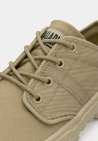 Μπεζ καμβά παπούτσι με στρογγυλά κορδόνια, μεταλλικά πλέγματα και υφή στην επιφάνεια. Διακοσμημένο με ετικέτα εμπορικού σήματος στον γιακά.