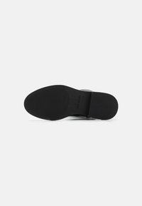 Suela de zapato de goma negra con una superficie texturizada y estriada para agarre. Presenta la marca "Steve Madden" cerca del talón. Bordes suaves.