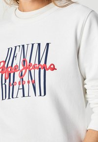 Felpa bianca con scritta audace blu navy e rossa "DENIM BRAND Pepe Jeans LONDON", con polsini a costine e scollo rotondo.