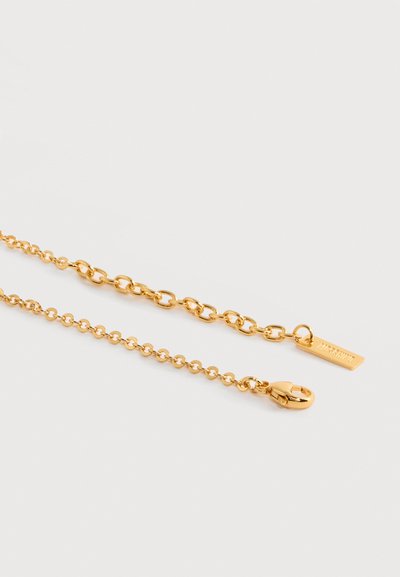 Δύο άκρα χρυσής αλυσίδας, το ένα με κούμπωμα αστακού, το άλλο με ορθογώνια ετικέτα χαραγμένη με όνομα μάρκας.